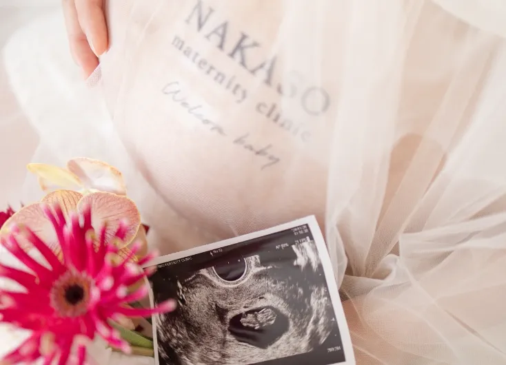 妊婦のお腹とエコー写真が写っており、花と布が添えられたシーン