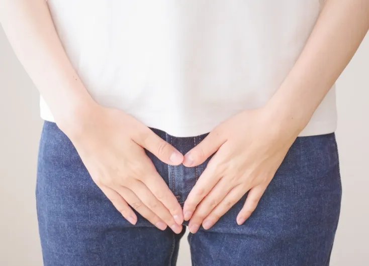 白いシャツとデニムを履いた女性が、股間部分を両手で覆っている写真。不正出血やデリケートゾーンの悩みを表現している。
