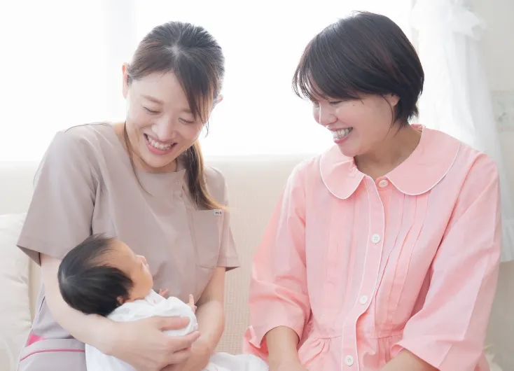出産後の赤ちゃんと看護師さんが抱いていて、お母さんが笑顔の様子